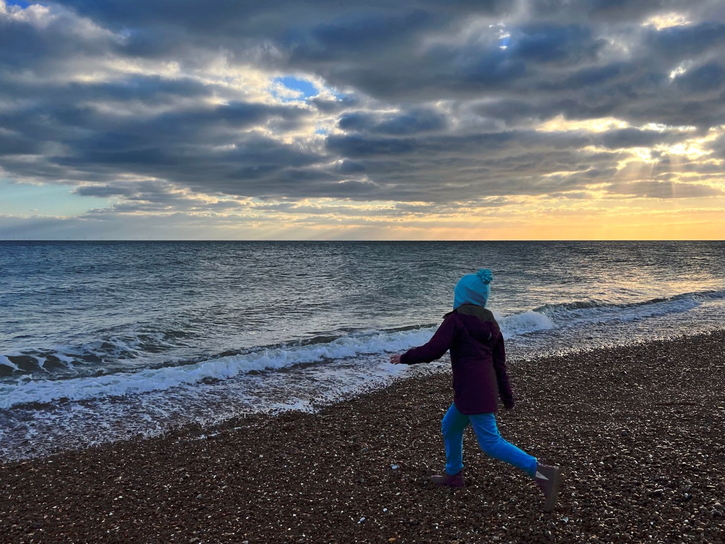 A young girl throwing a stone into the sea on a cold winter beach. 